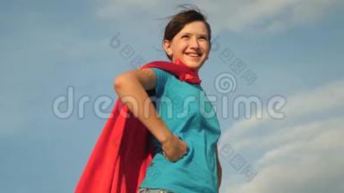 少女超级英雄穿着红色斗篷站在田野上，斗篷迎风飘扬。 慢动作。 女孩的梦想